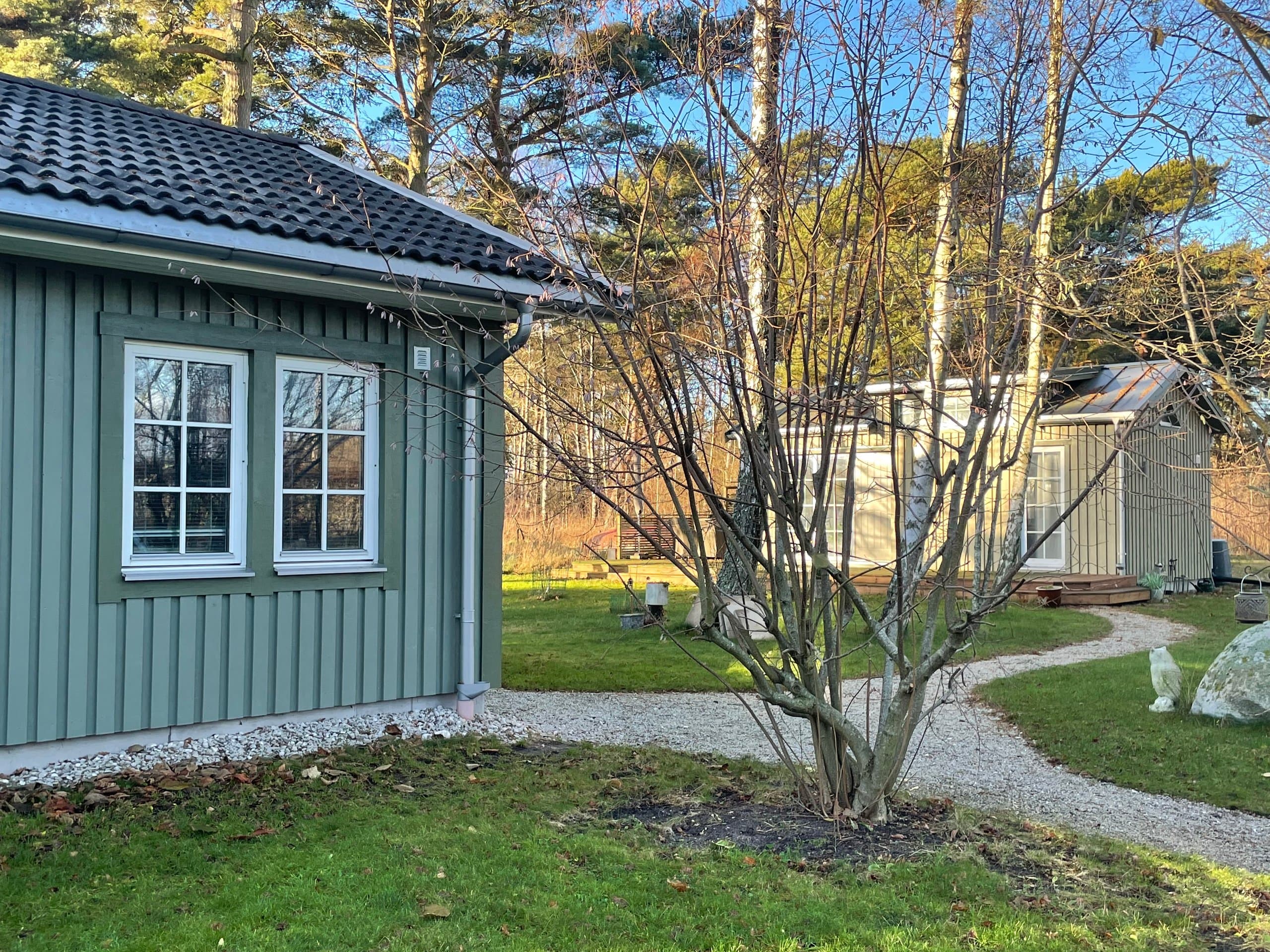 Hamngardi omgiven av naturen - charmig grön stuga med moderna fönster, vacker trädgård och grusvägar. En mysig retreat i lantlig miljö perfekt för avkoppling och naturupplevelser.